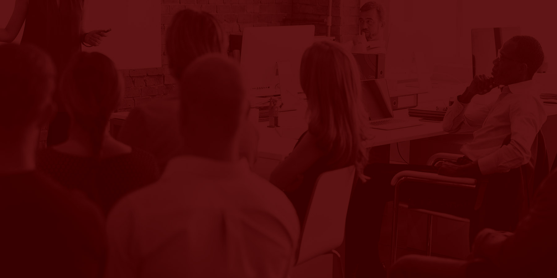 group of individuals sitting in a classroom listening to a presentation. Image is overlaid in maroon